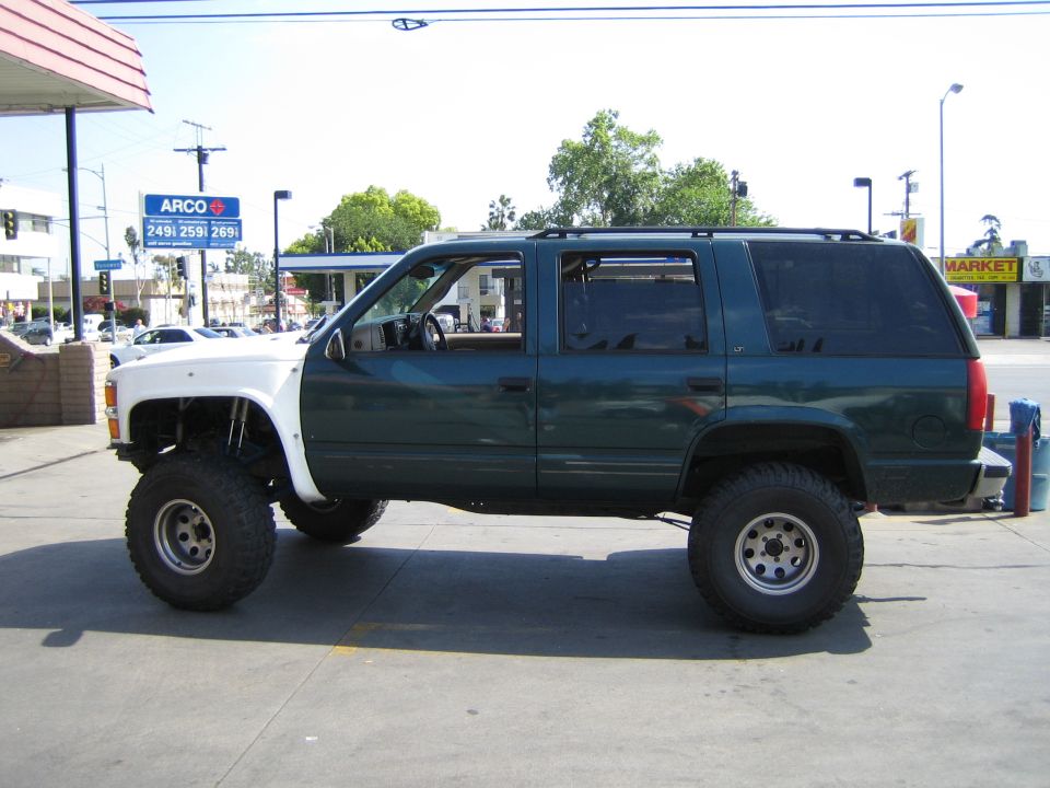 Green and white lifted Chevrolet Tahoe parked at a gas station, side view