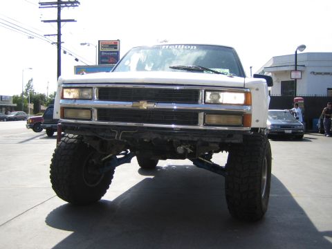 1990 Ford Bronco - Head-on view of a tall lifted Chevrolet with a chrome grille, bowtie emblem, and big off-road tires in a lot.