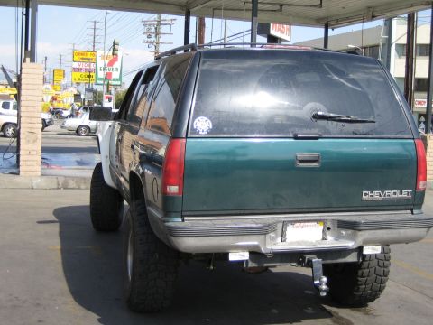 1990 Ford Bronco - Rear three-quarter view of a lifted green Chevrolet SUV with CHEVROLET lettering on the tailgate and a tow hitch, parked under a canopy.