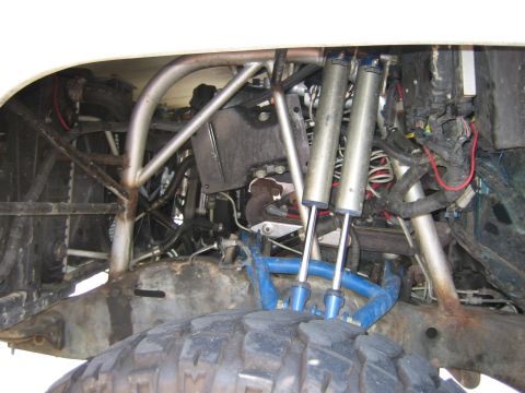 1990 Ford Bronco - Close-up of a vehicle undercarriage showing a custom tubular suspension with twin blue coilover shocks and blue control arms.