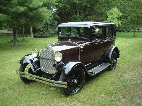1929 Ford Model A - This 1929 Ford Model A sedan is shown in a three-quarter front view, parked on a grassy lawn with trees in the background.