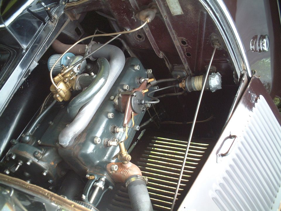 Vintage inline-four engine with brass carburetor and gray block in maroon engine bay