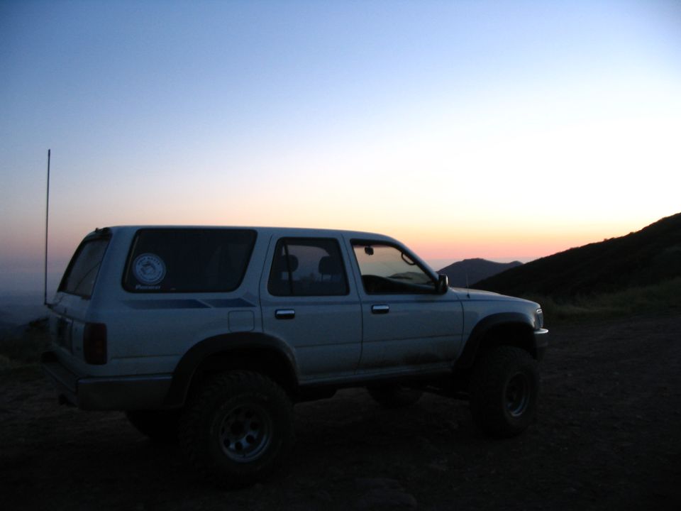 White lifted Toyota 4Runner on a dirt ridge at dusk silhouetted against an orange sky