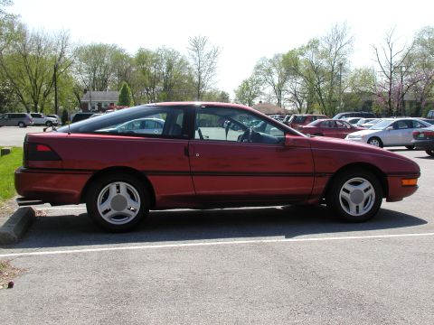 1991 Ford Probe - A red coupe is parked in a lot, showing its side profile with a distinctive sloping roofline.