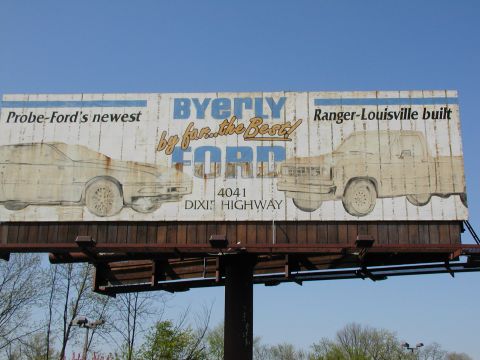 1991 Ford Probe - Billboard advertises Byerly Ford, illustrations of a car and a Ranger truck, with dealership address.