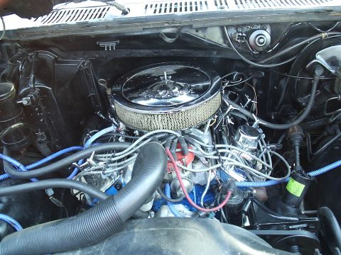 1985 Ford Bronco - Wide overhead engine bay view of a blue-block V8 topped with a chrome-lid Edelbrock air cleaner and white gauze filter. Blue plug wires, a…