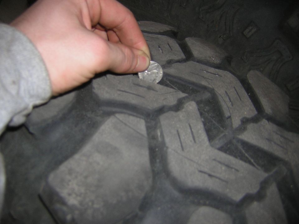hand holding quarter to measure tread depth on a large tire