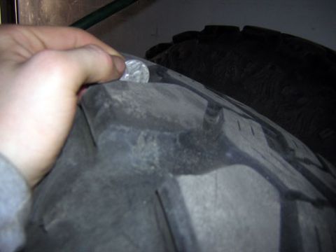 1995 Ford Bronco - A hand holds a quarter to measure the tread depth on a tire.