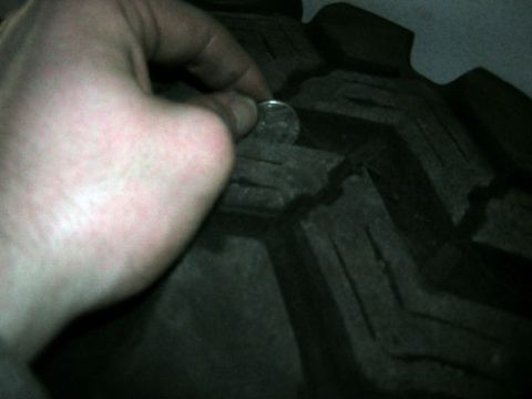1995 Ford Bronco - A coin is used to show the depth of the tire tread in this close-up view.