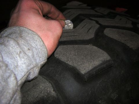 1995 Ford Bronco - A person is checking the tread depth of a tire using a coin.