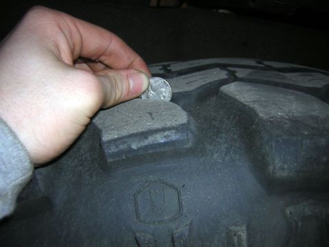 1995 Ford Bronco - A hand is shown holding a coin on the tread of a tire, likely to check tread depth.