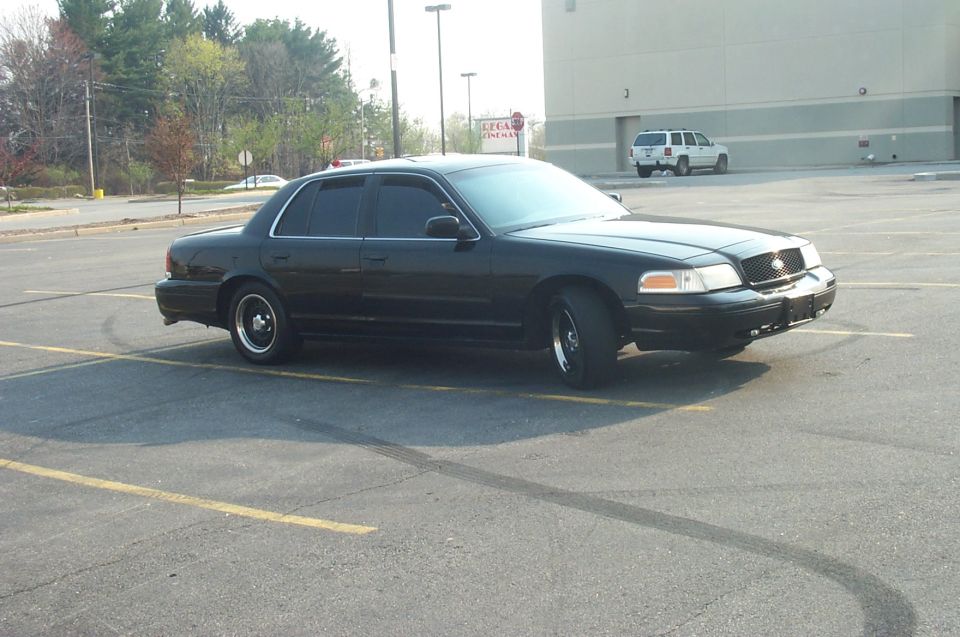 Black sedan parked in a lot, 3/4 front view. Aftermarket wheels and tinted windows are visible