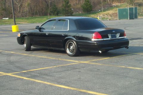 1999 Ford Crown Victoria - Three-quarter rear view of a lowered black Ford Crown Victoria sedan sitting in an empty asphalt parking lot with yellow stall lines and a…