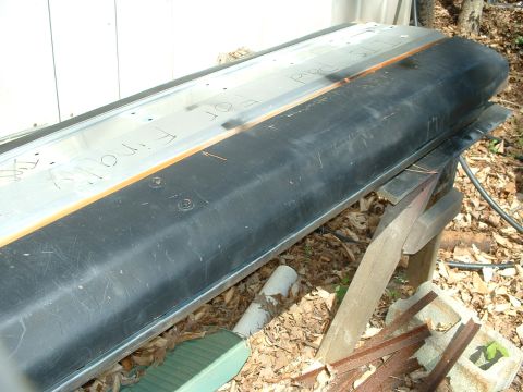 1985 Ford Bronco - A vehicle part rests on wooden supports outdoors, with handwritten text visible on its surface.
