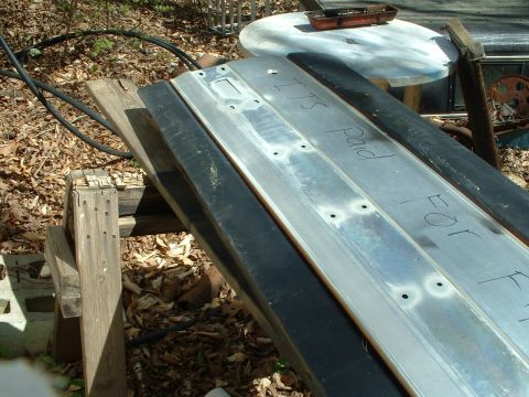 1985 Ford Bronco - Metal parts with handwritten text are resting on wooden supports outdoors.