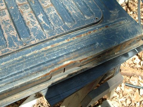 1985 Ford Bronco - A close-up view of a damaged and rusted vehicle tailgate, showing significant wear and tear.
