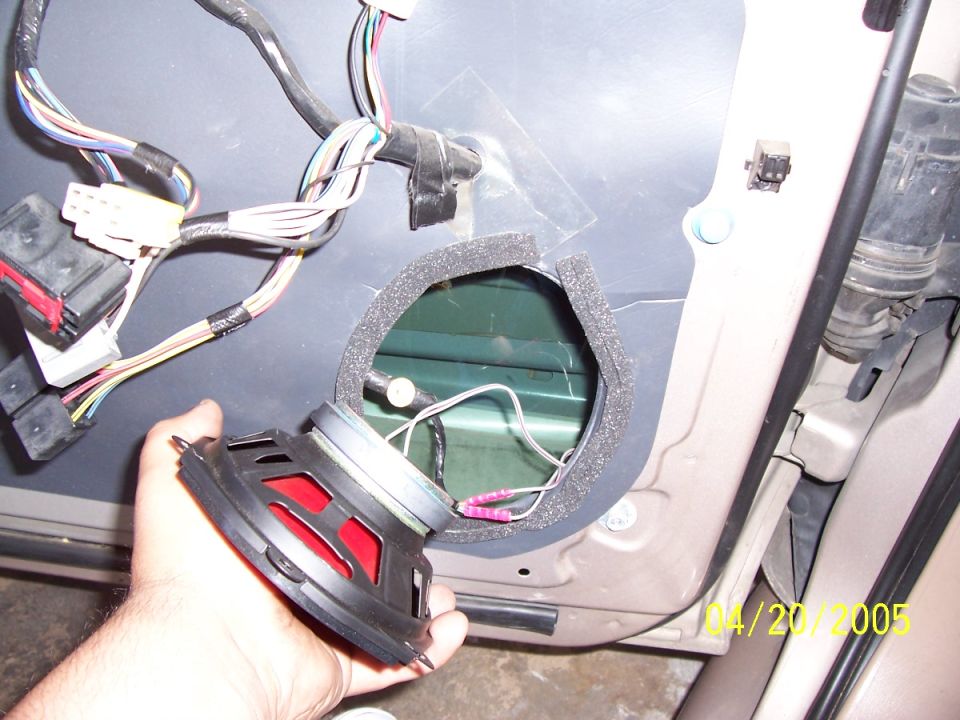 Car door panel removed, showing wiring harness and speaker removed from its mounting hole