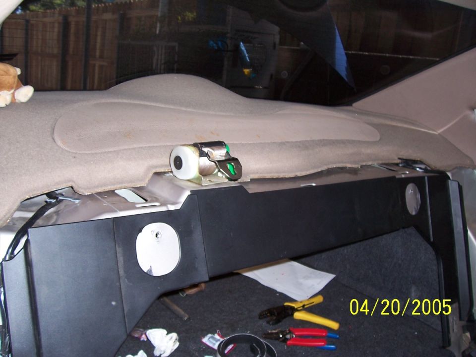 Car interior rear deck with a black speaker box, tools, and a seatbelt anchor. Date stamp reads 04/20/2005