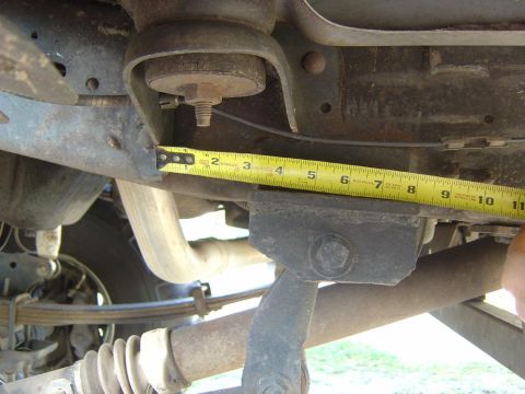 1993 Ford Bronco - A yellow tape measure is used to measure a section of the vehicle's frame, showing suspension components and exhaust pipe.