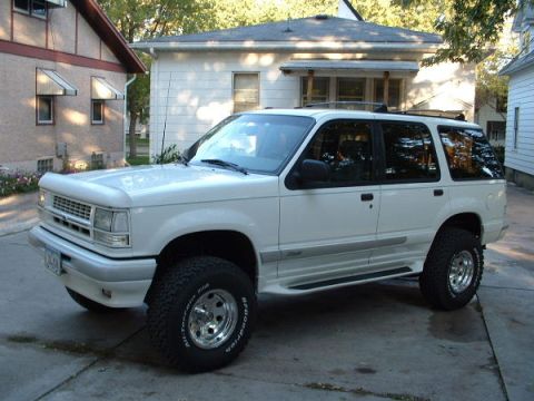 1991 Ford Explorer - This white Ford Explorer is parked in front of a residential house. The vehicle has a roof rack and running boards.