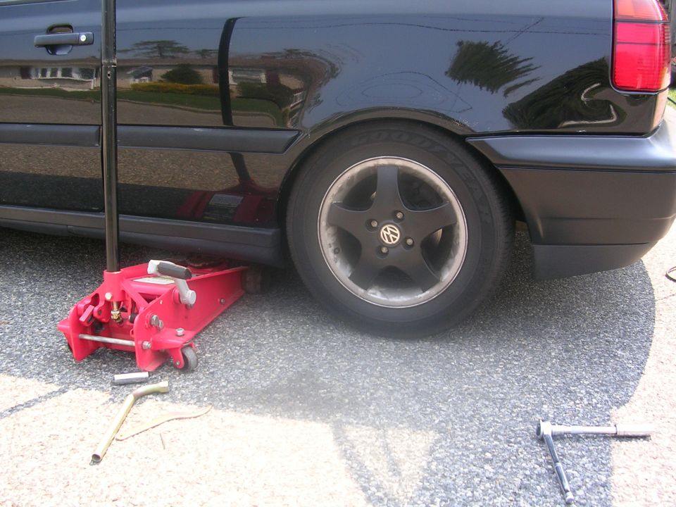 1996 Volkswagen GTI with a red floor jack under the rear wheel, lug wrench on the ground