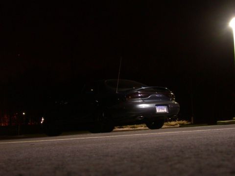 1997 Ford Taurus - A dark sedan is parked at night, illuminated by a street light.