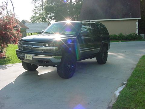 2000 Chevrolet Tahoe - This dark SUV, likely a 2000 Chevrolet Tahoe, is shown from a 3/4 front angle with aftermarket wheels.