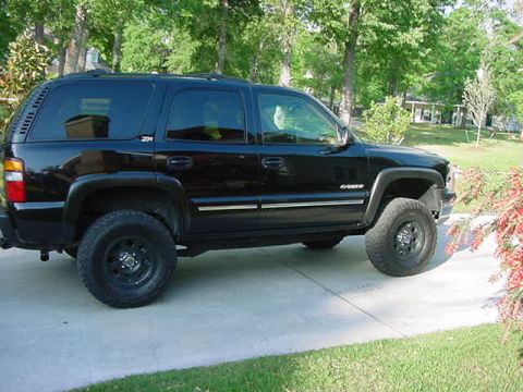 2000 Chevrolet Tahoe - A black Chevrolet Tahoe is seen from the side, parked on a concrete driveway with trees in the background.