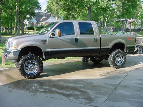 2000 Chevrolet Tahoe - A lifted pickup truck is parked on a wet concrete surface, towing a boat trailer.