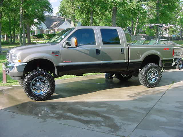Lifted pickup truck towing a boat trailer, parked on a concrete driveway