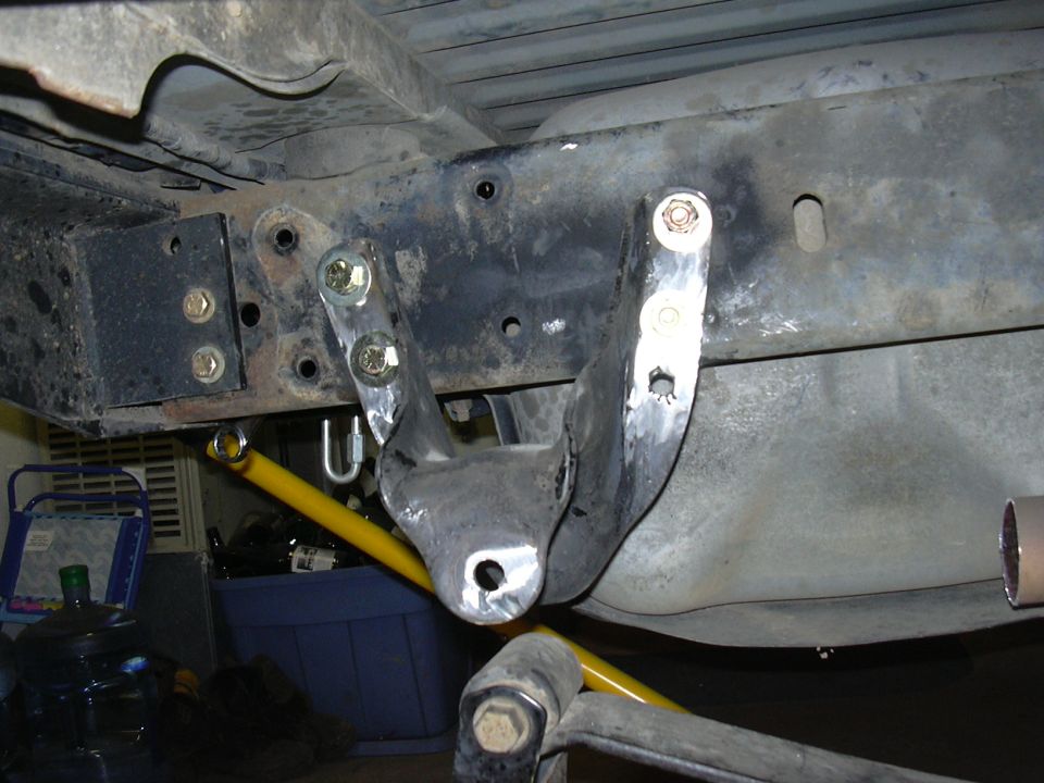 Underbody frame with welded bare-metal bracket, bolts, and yellow suspension link
