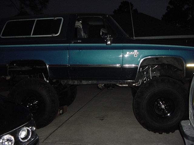 Lifted teal and black Chevrolet Blazer SUV with big off-road tires, side view at night on a driveway