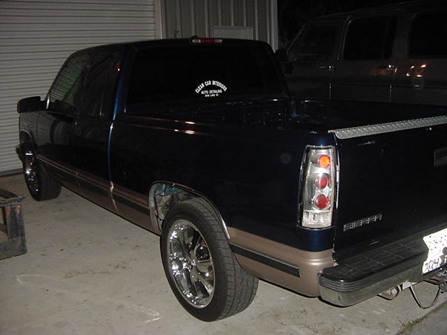 Dark two-tone GMC Sierra extended-cab pickup with chrome wheels and clear tail lights in a garage