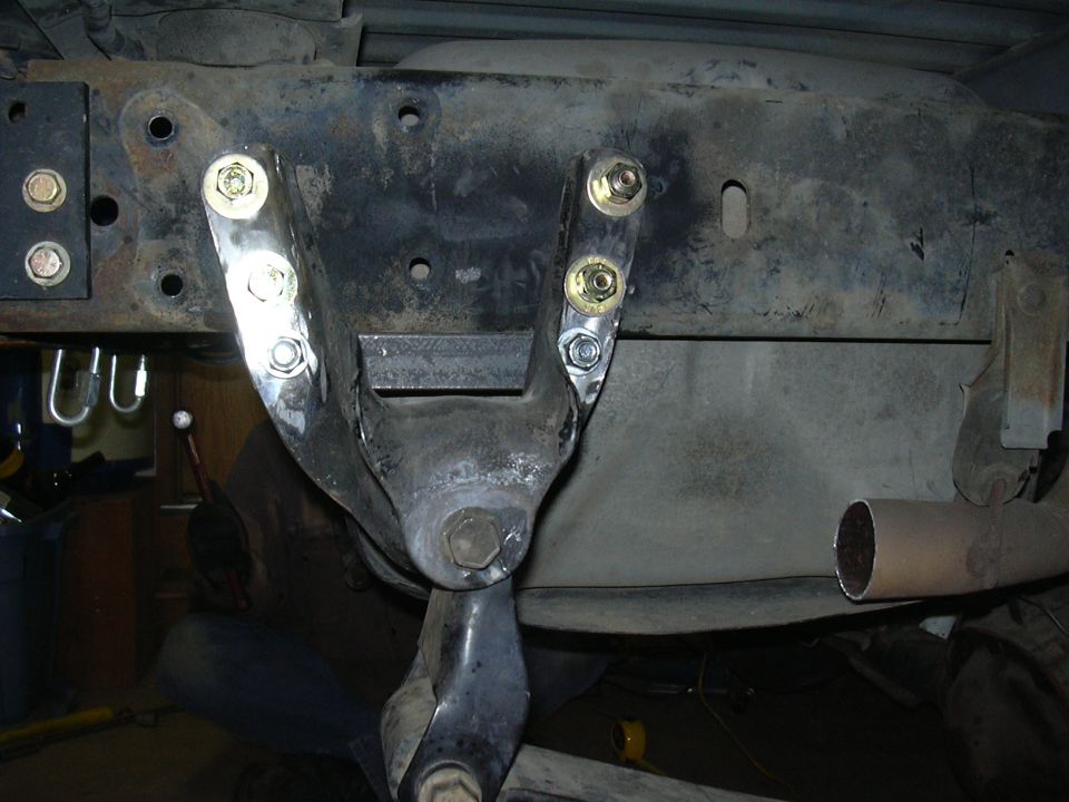 Steel bracket bolted to vehicle frame underside with new bolts, exhaust pipe at right