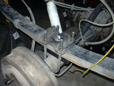 1991 Ford Bronco - Close-up of a leaf spring rear axle suspension viewed from underneath, showing a spring perch/plate with four threaded U-bolt studs and nut…