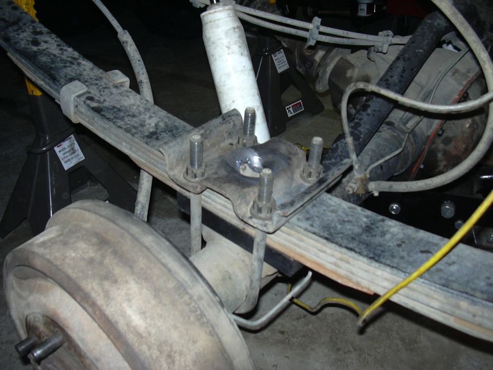 Underside view of leaf spring axle with U-bolt plate, white shock, and brake drum on jack stands