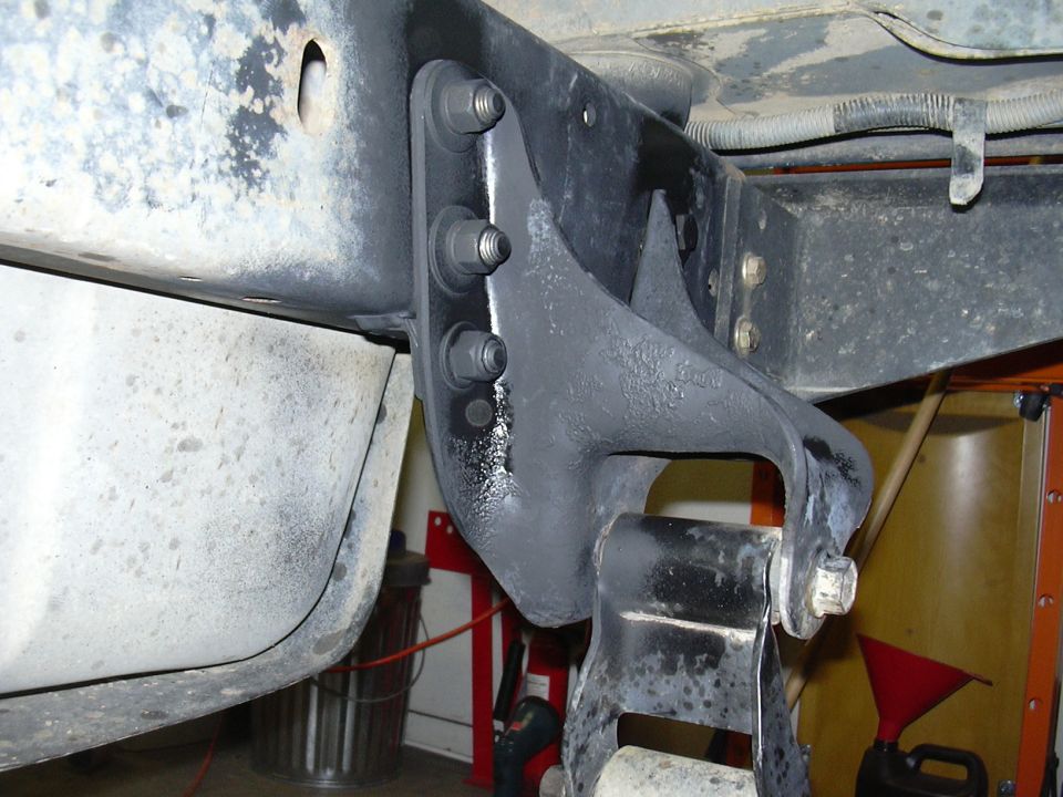 Gray-painted frame bracket with three bolts and black suspension hanger underneath a vehicle