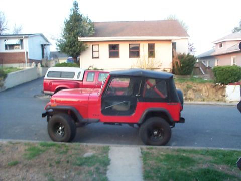 1989 Jeep YJ - A red Jeep CJ is parked on the street, with a red pickup truck and camper shell behind it.