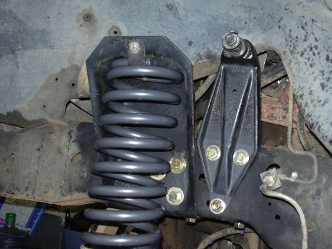 1991 Ford Bronco - Underbody view of a coil spring suspension component, showing a freshly painted black bracket holding a gray coil spring, with zinc-plated…