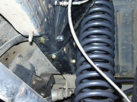 1991 Ford Bronco - Underbody view of a coil spring suspension showing a dark blue/gray coil spring, a bracket held by several bolts with yellow-zinc washers,…