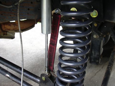 1991 Ford Bronco - Close-up of a front suspension showing a gray coil spring, a silver shock absorber, and a red limiting strap mounted to a black frame brack…