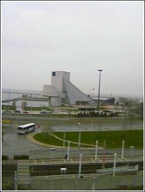 1993 Ford Bronco - A white bus drives on a wet road in front of a modern building with a large glass facade.