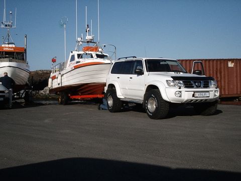 1996 Ford Bronco - A white Nissan Patrol SUV is parked next to a boat on a trailer under a clear blue sky.