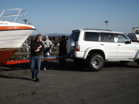 1996 Ford Bronco - A white SUV is parked next to a boat on a trailer, with people standing around.