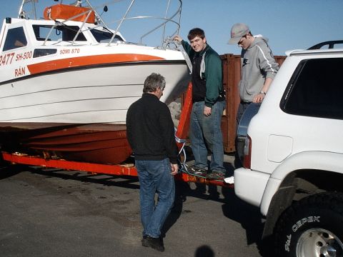 1996 Ford Bronco - A white SUV is parked next to a trailer carrying a boat, with several people around.