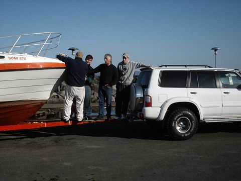 1996 Ford Bronco - A group of men stand near a white SUV and a boat on a trailer by the water.