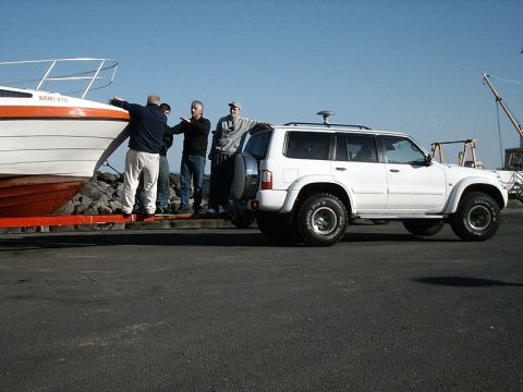 1996 Ford Bronco - White SUV is parked next to a boat on a trailer, with people standing around.
