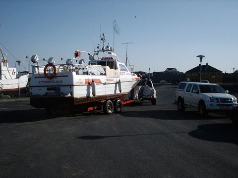 1996 Ford Bronco - A white SUV tows a boat on a trailer in a harbor area with other vessels visible.
