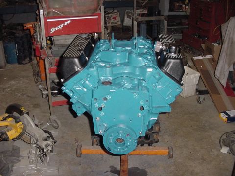 1969 Ford Bronco - A turquoise V8 engine is mounted on an engine stand in a garage, surrounded by tools and equipment.