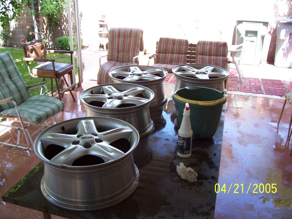 Four aluminum alloy wheels and cleaning supplies on a table outdoors